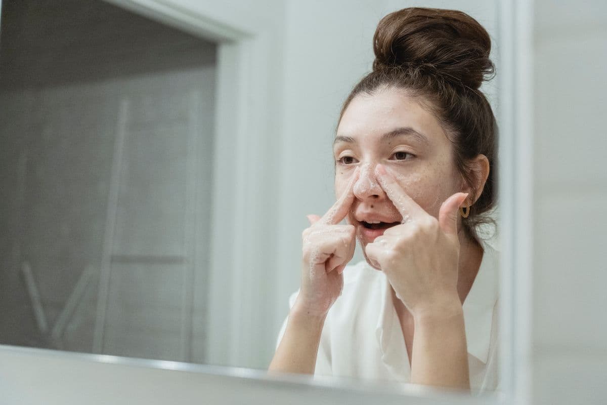 Banyo aynasının önünde yüzünü köpükle temizleyen bir kadın