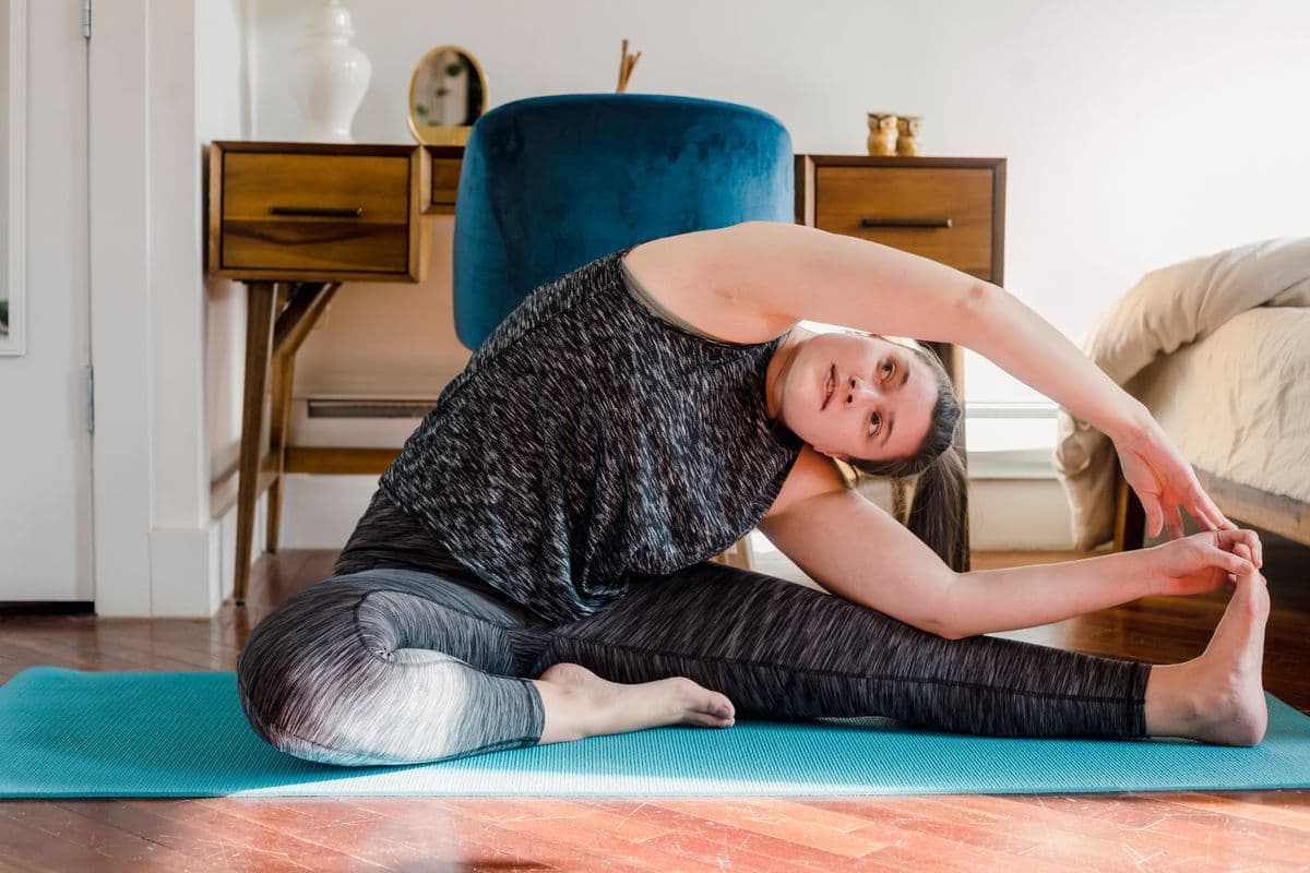 Evde yoga minderi üzerinde esneme ve denge hareketi yapan bir kadın